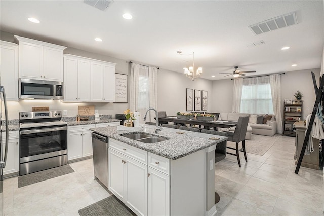 kitchen featuring light stone countertops, stainless steel appliances, a kitchen island with sink, sink, and white cabinets