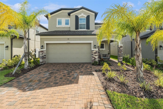 view of front of home featuring an attached garage, stone siding, decorative driveway, and stucco siding