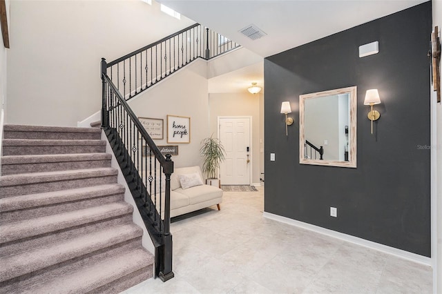 foyer featuring visible vents, a towering ceiling, baseboards, and stairs