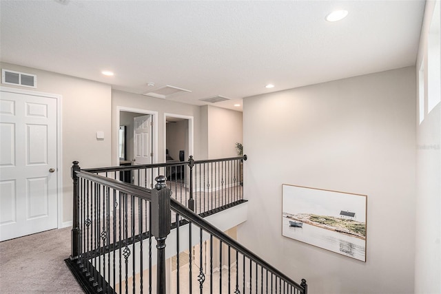 hallway with carpet, visible vents, and an upstairs landing