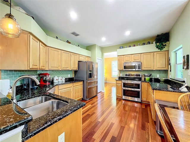 kitchen featuring dark stone counters, sink, hanging light fixtures, light hardwood / wood-style flooring, and appliances with stainless steel finishes