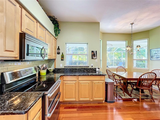 kitchen with appliances with stainless steel finishes, dark stone counters, a healthy amount of sunlight, a notable chandelier, and hanging light fixtures