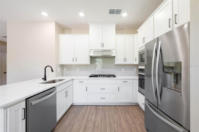 kitchen featuring appliances with stainless steel finishes, light wood-type flooring, tasteful backsplash, light stone counters, and white cabinets