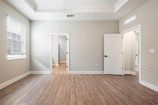 spare room featuring a tray ceiling, light hardwood / wood-style flooring, plenty of natural light, and ornamental molding