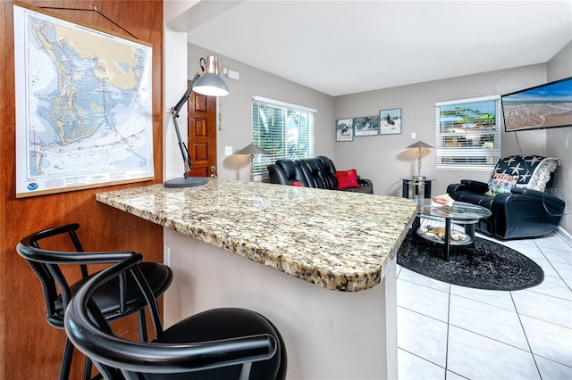 kitchen featuring light tile patterned flooring, light stone counters, and a breakfast bar area