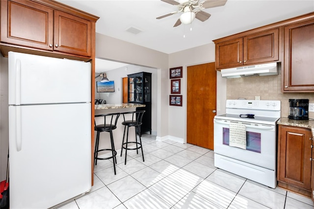 kitchen featuring ceiling fan, a kitchen breakfast bar, tasteful backsplash, white appliances, and light tile patterned floors