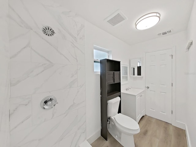 bathroom featuring hardwood / wood-style flooring, vanity, toilet, and a tile shower