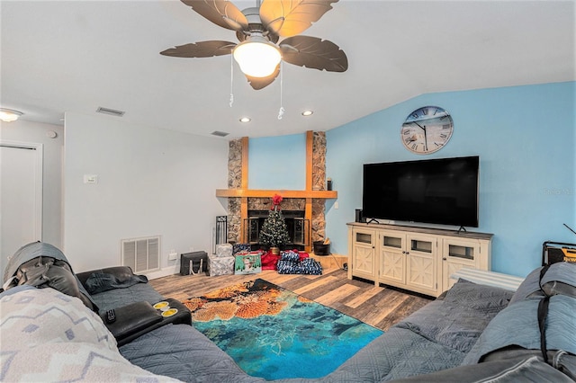 living room with hardwood / wood-style flooring, a stone fireplace, and lofted ceiling