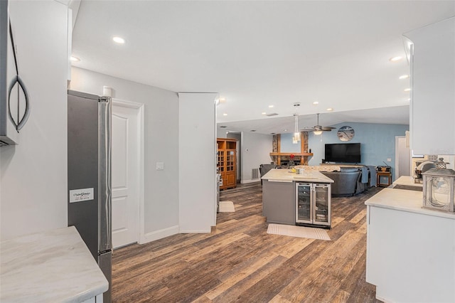 kitchen with beverage cooler, dark wood-type flooring, ceiling fan, white cabinets, and stainless steel refrigerator