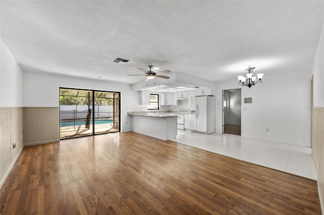 unfurnished living room with ceiling fan with notable chandelier, sink, a textured ceiling, and light hardwood / wood-style flooring