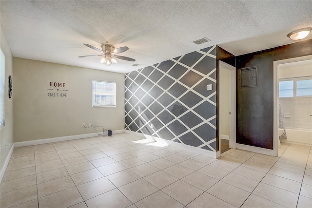 empty room with ceiling fan, light tile patterned floors, a textured ceiling, and tile walls