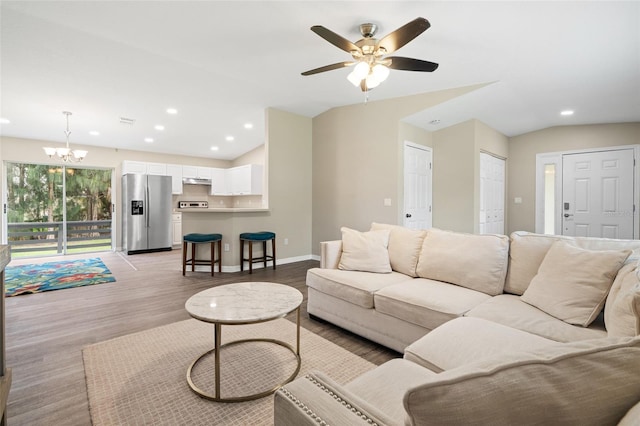 living room featuring ceiling fan with notable chandelier, light hardwood / wood-style floors, and vaulted ceiling