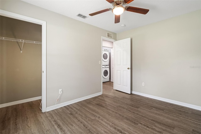 unfurnished bedroom featuring a closet, dark wood-type flooring, ceiling fan, and stacked washer / drying machine