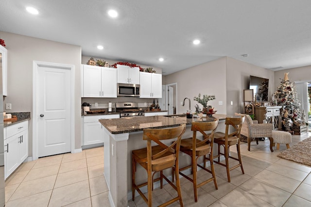 kitchen with dark stone counters, sink, an island with sink, white cabinetry, and stainless steel appliances