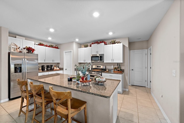 kitchen with a kitchen bar, a kitchen island with sink, appliances with stainless steel finishes, and dark stone counters