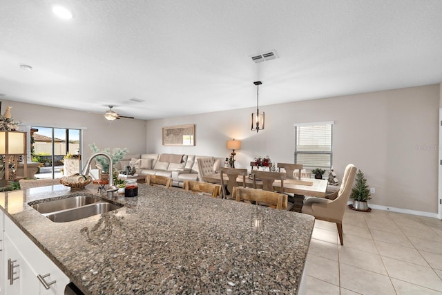 kitchen with a center island with sink, decorative light fixtures, sink, and dark stone counters