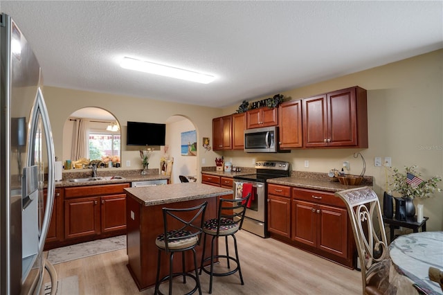 kitchen with light wood-type flooring, appliances with stainless steel finishes, a center island, and sink