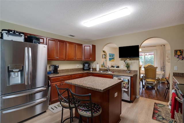 kitchen featuring appliances with stainless steel finishes, a textured ceiling, sink, a center island, and light hardwood / wood-style floors