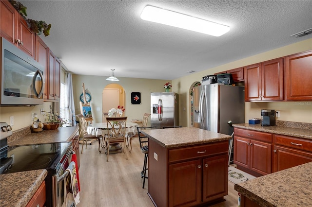 kitchen with a center island, pendant lighting, light hardwood / wood-style floors, a textured ceiling, and appliances with stainless steel finishes