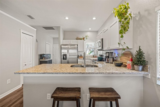 kitchen with kitchen peninsula, sink, appliances with stainless steel finishes, dark hardwood / wood-style flooring, and white cabinetry