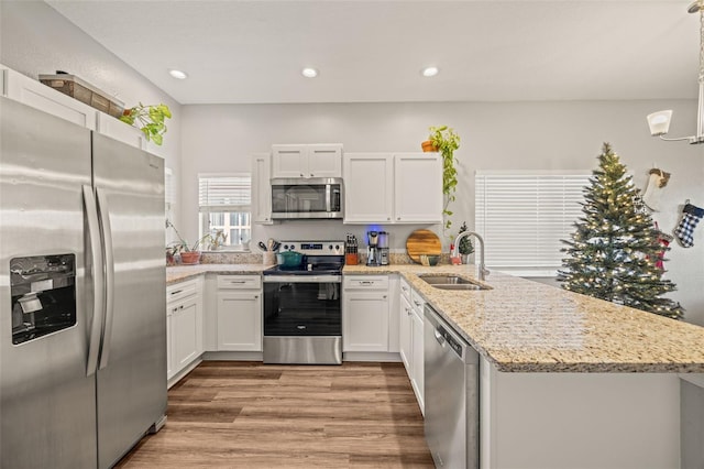 kitchen with sink, appliances with stainless steel finishes, decorative light fixtures, light hardwood / wood-style floors, and white cabinetry