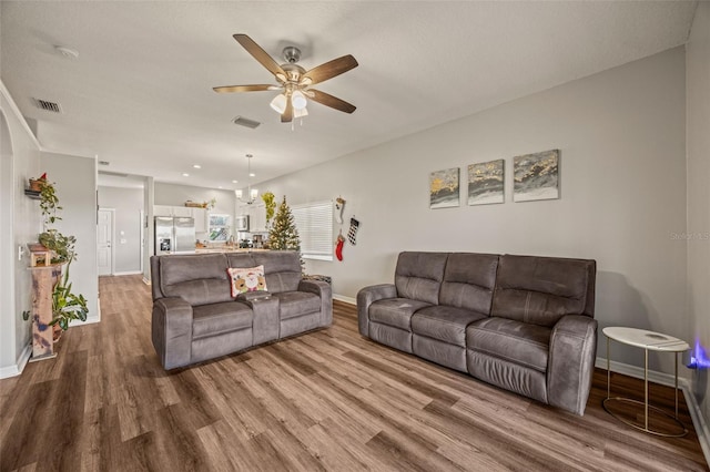 living room with hardwood / wood-style flooring, ceiling fan with notable chandelier, and a textured ceiling