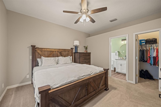 bedroom with ceiling fan, light colored carpet, a walk in closet, and connected bathroom