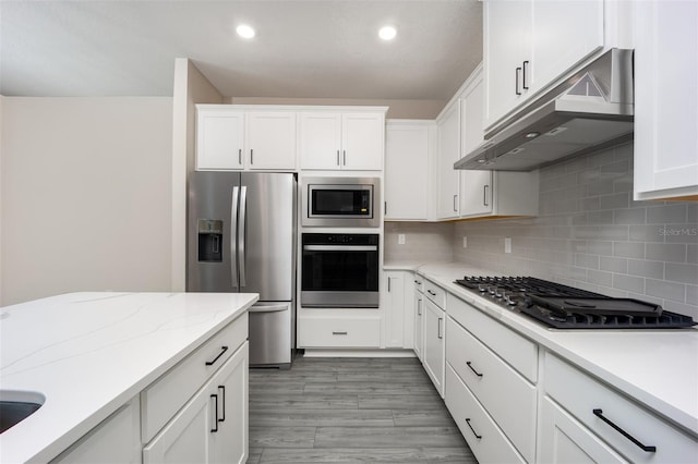 kitchen featuring backsplash, white cabinets, light hardwood / wood-style flooring, appliances with stainless steel finishes, and light stone counters