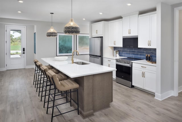 17390 Moonflower Dr Unit 102, Venice, FL 34293 - kitchen with stainless steel appliances, an island with sink, a sink, light wood-type flooring, and backsplash