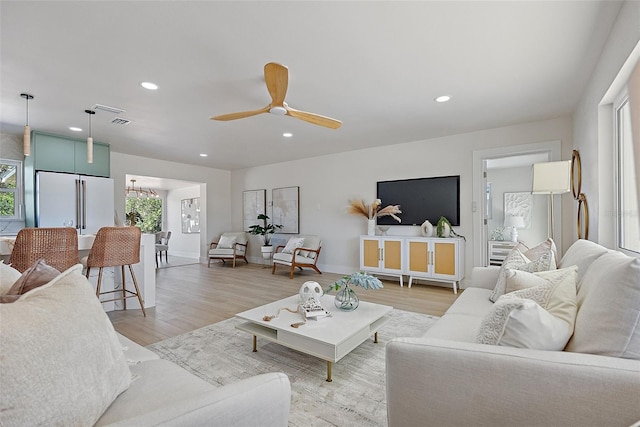 living room featuring ceiling fan with notable chandelier and light hardwood / wood-style floors