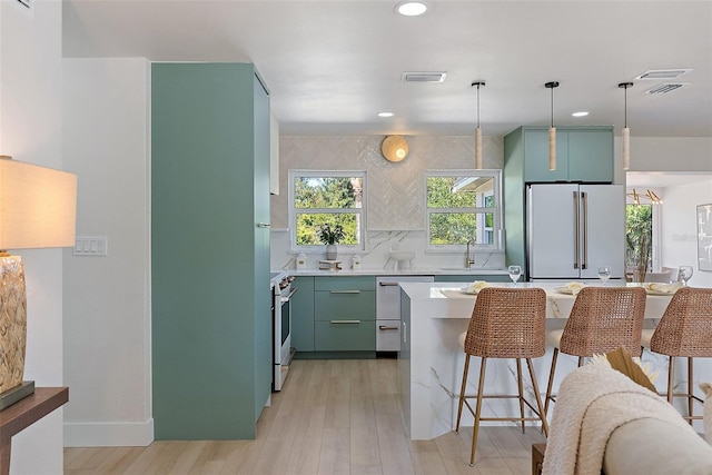 kitchen with white appliances, decorative light fixtures, a breakfast bar area, light hardwood / wood-style floors, and green cabinets