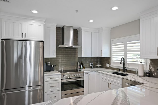 kitchen with white cabinets, appliances with stainless steel finishes, light stone counters, and wall chimney range hood