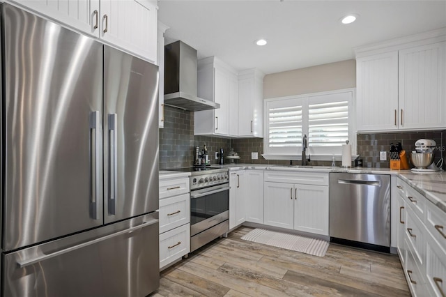 kitchen with white cabinets, light hardwood / wood-style floors, wall chimney range hood, and appliances with stainless steel finishes