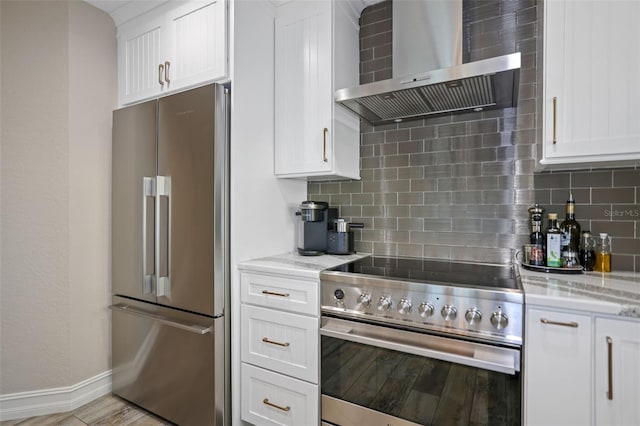 kitchen featuring wall chimney exhaust hood, stainless steel appliances, tasteful backsplash, light stone counters, and white cabinets