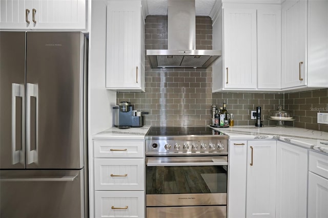 kitchen featuring light stone countertops, wall chimney exhaust hood, tasteful backsplash, white cabinets, and appliances with stainless steel finishes