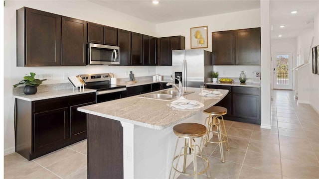 kitchen featuring a center island with sink, sink, dark brown cabinets, a kitchen bar, and stainless steel appliances