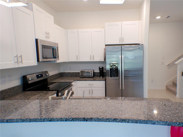 kitchen with white cabinets, appliances with stainless steel finishes, and dark stone countertops