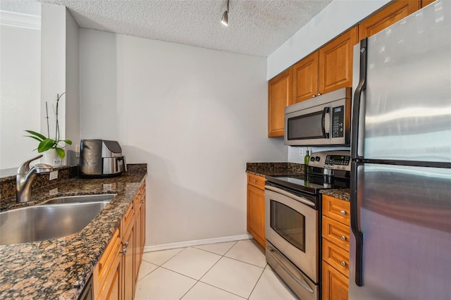 kitchen featuring appliances with stainless steel finishes, a textured ceiling, sink, light tile patterned floors, and dark stone countertops