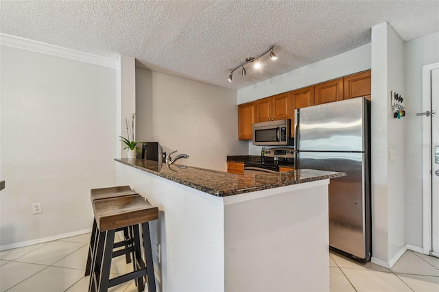 kitchen with a kitchen bar, kitchen peninsula, stainless steel appliances, and dark stone counters