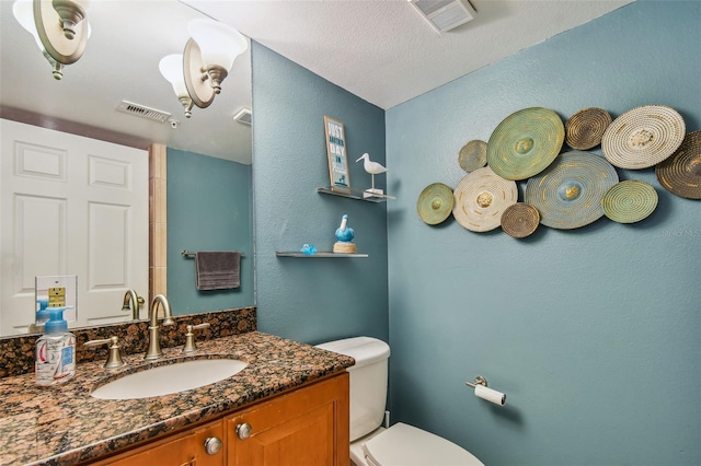 bathroom with a textured ceiling, vanity, and toilet