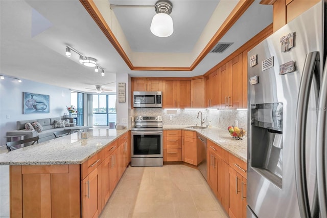 kitchen featuring light stone countertops, ceiling fan, stainless steel appliances, kitchen peninsula, and decorative backsplash