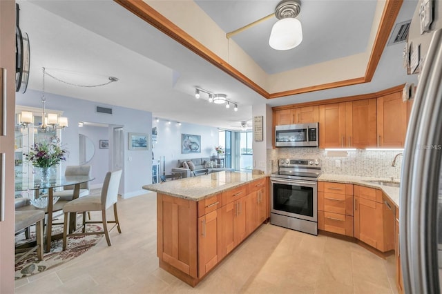 kitchen featuring decorative backsplash, light stone countertops, kitchen peninsula, stainless steel appliances, and a chandelier