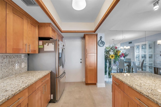 kitchen with stainless steel fridge, backsplash, decorative light fixtures, and light stone counters