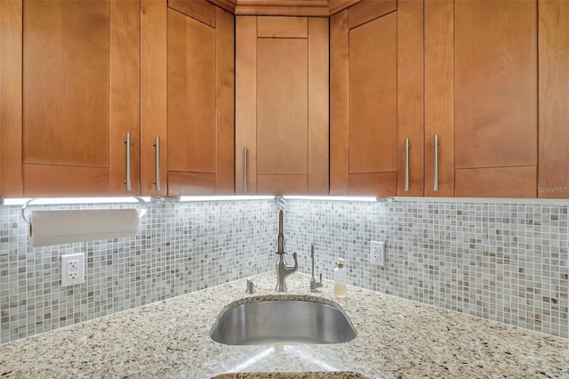 room details featuring sink, light stone countertops, and backsplash