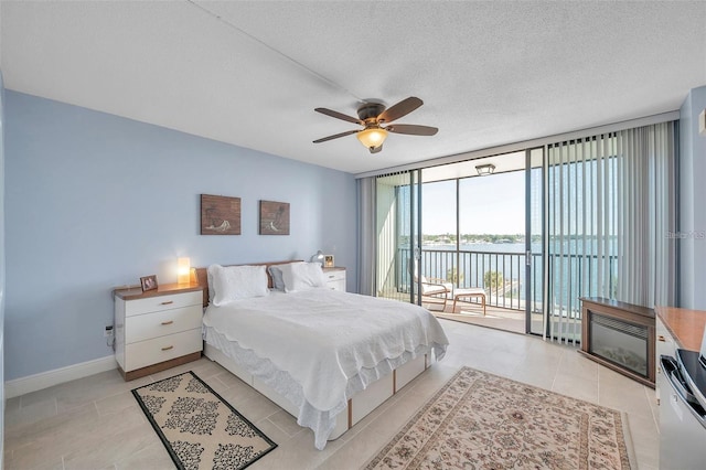 bedroom with access to exterior, ceiling fan, expansive windows, a textured ceiling, and a water view