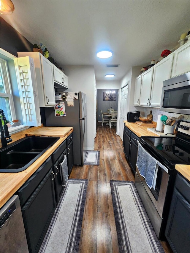 kitchen featuring appliances with stainless steel finishes, dark wood-type flooring, sink, butcher block countertops, and white cabinetry