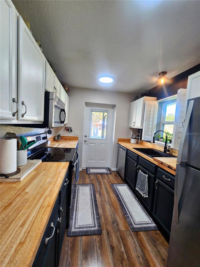 kitchen with sink, wooden counters, plenty of natural light, white cabinets, and appliances with stainless steel finishes