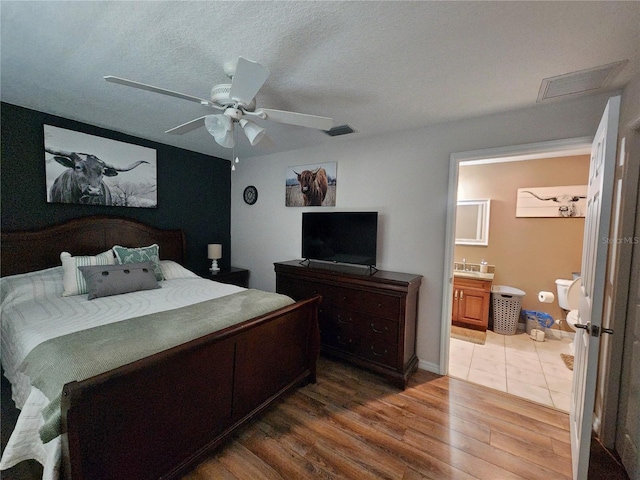 bedroom featuring ensuite bath, ceiling fan, hardwood / wood-style floors, and a textured ceiling