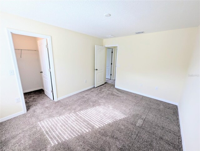 unfurnished bedroom with a textured ceiling, a walk in closet, carpet floors, and a closet