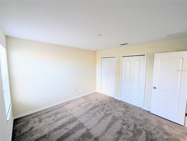 unfurnished bedroom featuring carpet flooring, a textured ceiling, and multiple closets